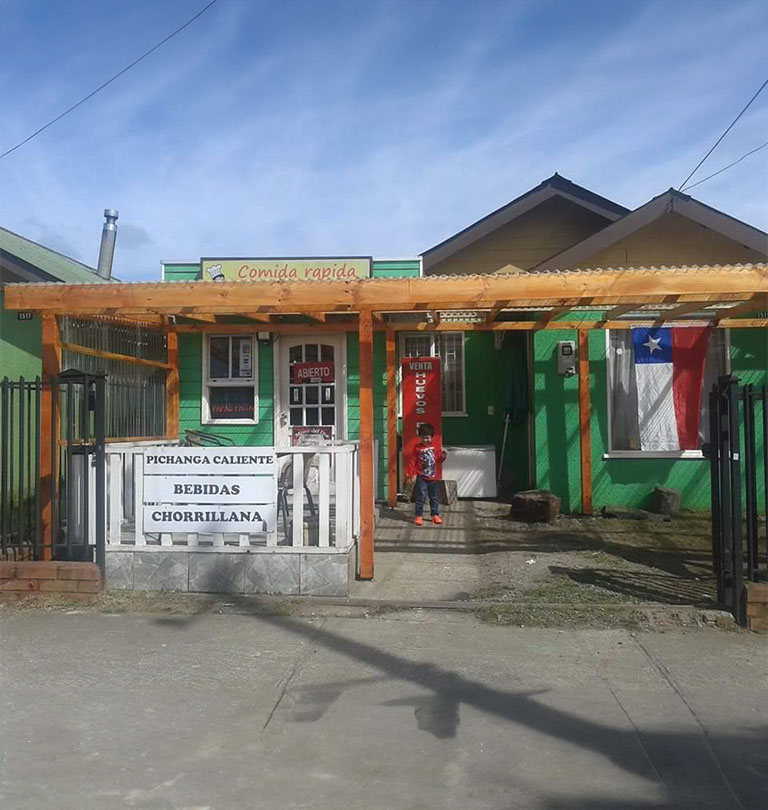 Es una casa con una fachada verde y puerta blanca, ya más avanzada en su arquitectura en el cual se aprecia un techo de madera con diversos carteles de venta de comida rápida y el principal que dice "Comida rápida El Sabrosón"