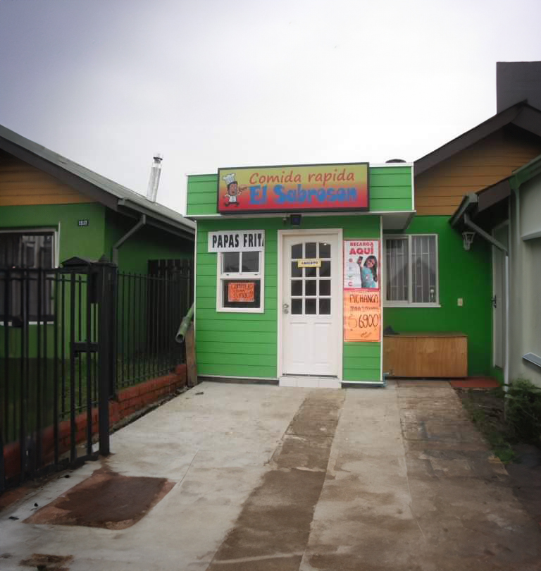 Es una casa con una fachada verde y puerta blanca, ya más avanzada en su arquitectura en el cual se aprecia un techo de madera con diversos carteles de venta de comida rápida y el principal que dice "Comida rápida El Sabrosón"